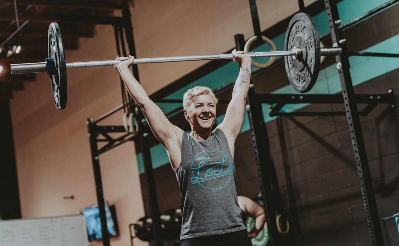 middle aged woman lifts olympic barbell in crossfit gym in victoria bc wearing crossfit lolo muscle t